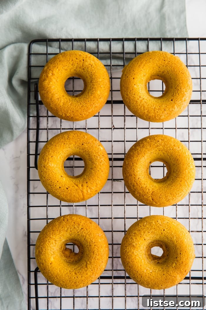 Spiced Pumpkin Donut Delights 7 Baked vegan pumpkin donuts cooling on a wire rack on a green kitchen towel, ready for coating.