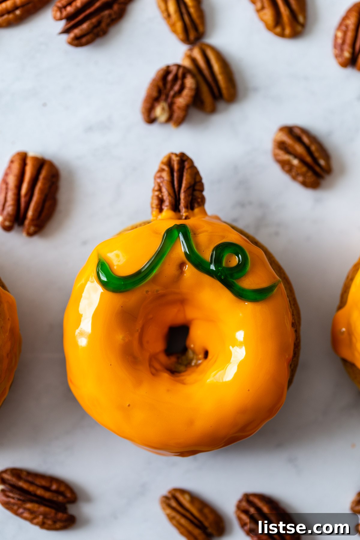 Spiced Pumpkin Donut Delights 8 Decorated pumpkin-shaped vegan donuts with pecan stems and green icing leaves.