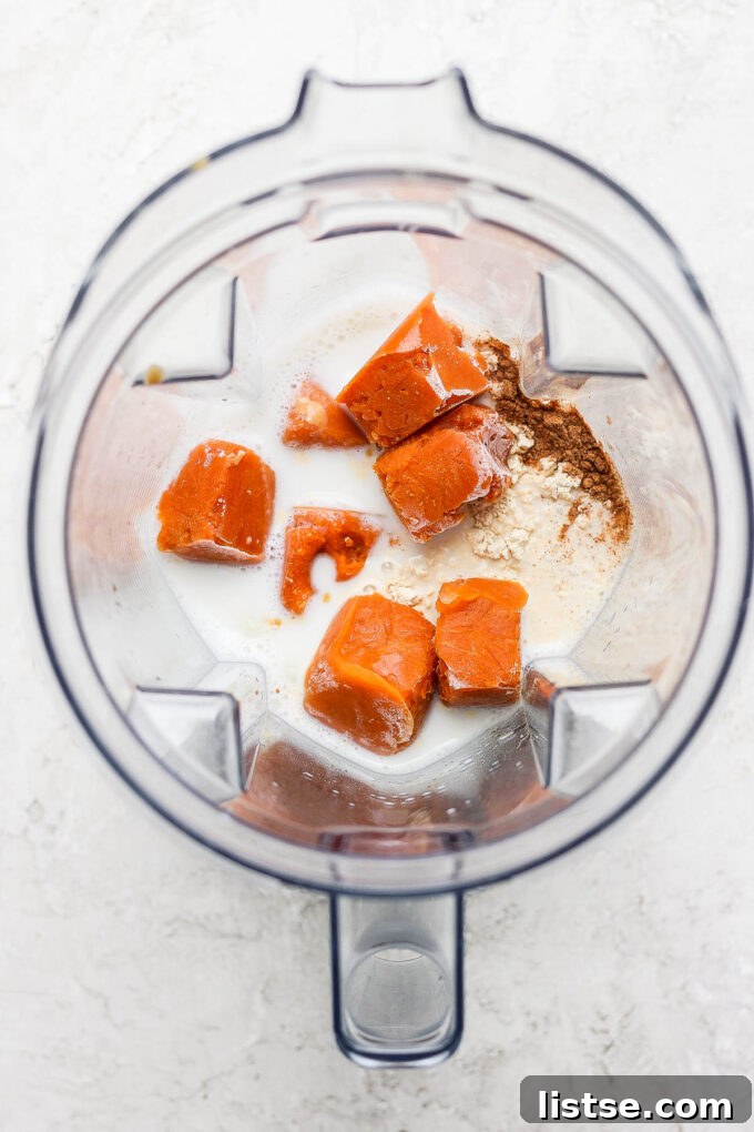 Adding cubed pumpkin and milk to a blender, beginning the smoothie preparation.