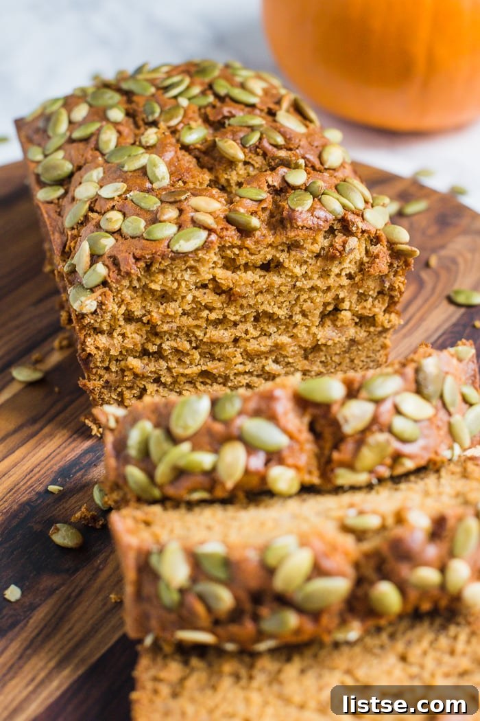 Plant-Based Pumpkin Spice Loaf 2 A slice of moist vegan pumpkin bread with baked-on pepitas, showing its tender crumb, with a whole pumpkin in the background.