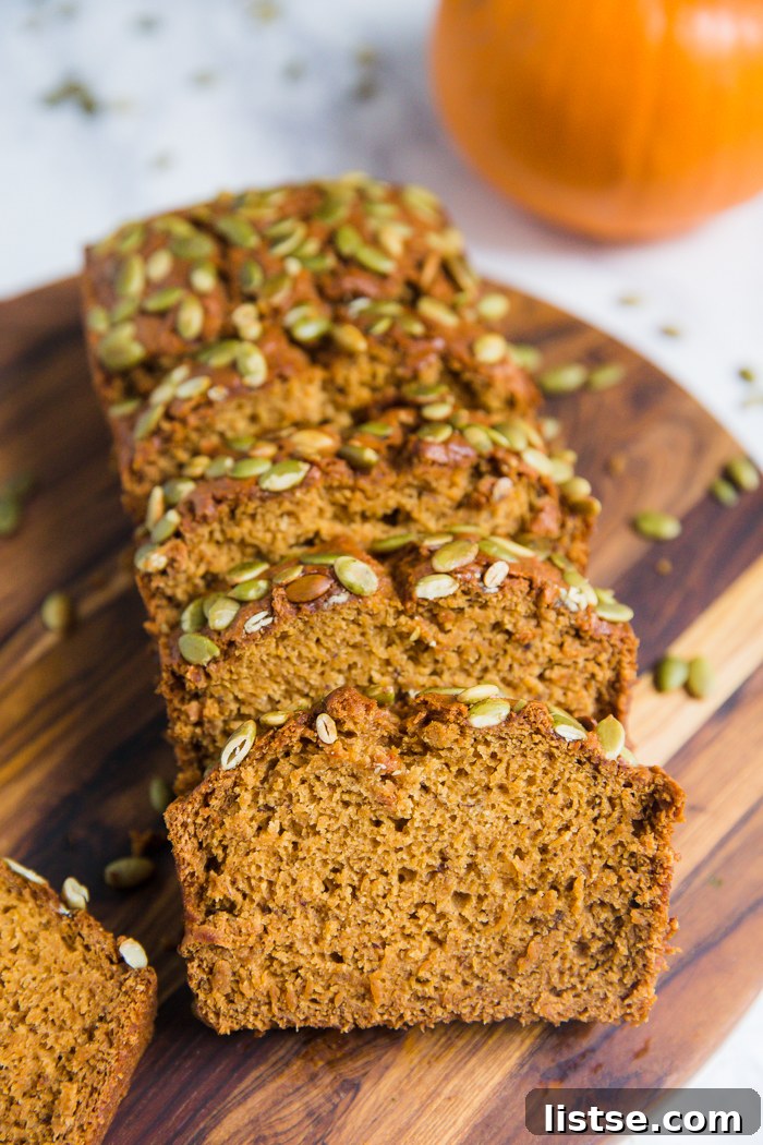 Plant-Based Pumpkin Spice Loaf 4 A beautifully sliced vegan pumpkin bread revealing its soft, moist interior and golden crust topped with pepitas, with a decorative pumpkin nearby.