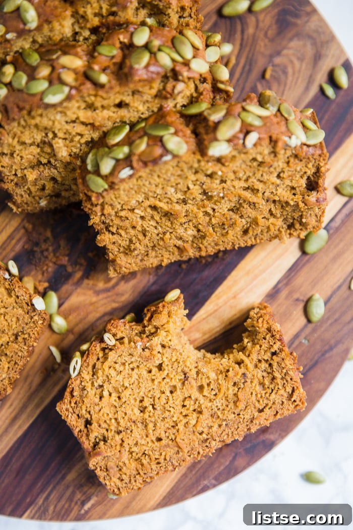 Plant-Based Pumpkin Spice Loaf 7 A sliced vegan pumpkin bread loaf, showcasing its fluffy texture and inviting color, with pepitas on top, and pumpkins in the background.