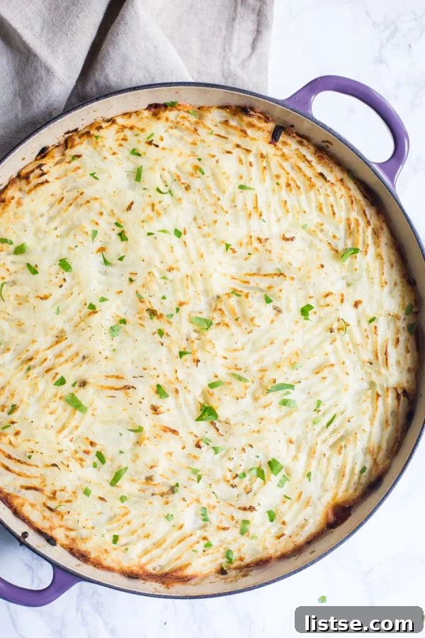 A beautifully presented vegetarian pot pie, generously topped with fluffy mashed potatoes. The potato topping shows charming fork indentations, indicating its fresh preparation. The pie is served in a distinct purple skillet, resting elegantly on a sophisticated marble board, ready to be enjoyed.