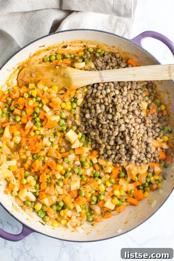 A close-up shot of cooked lentils and sautéed vegetables perfectly combined inside a striking purple skillet, with a wooden spoon resting nearby. The vibrant colors of the vegetables and the rich texture of the lentils indicate a hearty and flavorful dish in preparation.