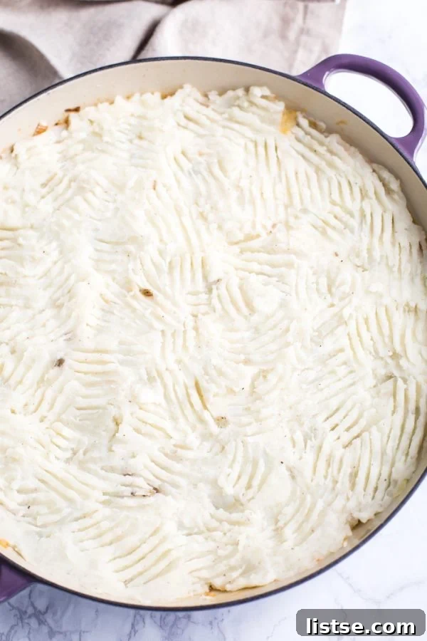 A beautifully presented vegetarian pot pie, generously topped with fluffy mashed potatoes. The potato topping shows charming fork indentations, indicating its fresh preparation. The pie is served in a distinct purple skillet, resting elegantly on a sophisticated marble board, ready to be enjoyed.