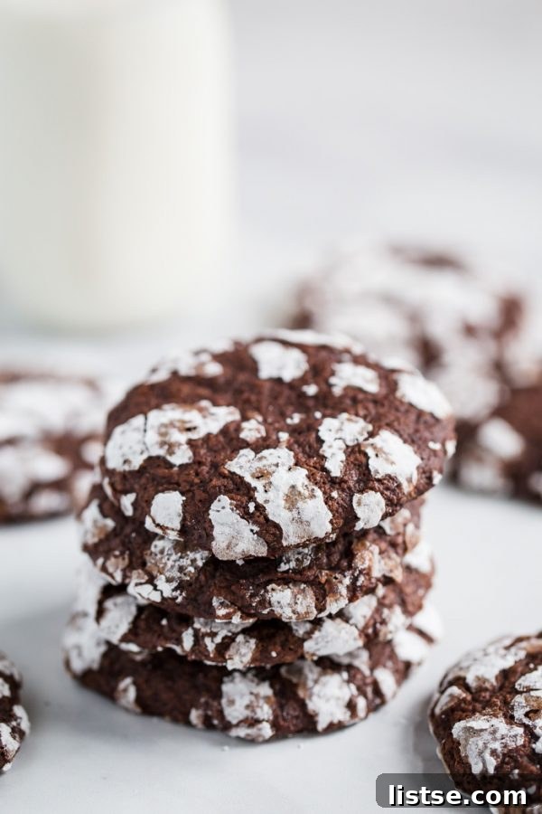 A batch of freshly baked vegan chocolate crinkle cookies cooling on a wire rack, glistening with powdered sugar.