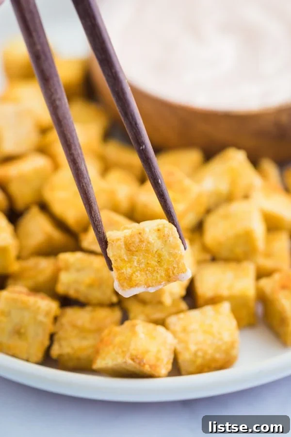 Crispy Golden Tofu Perfection 2 crispy tofu cubes on a large plate with one being held up by a wooden pair of chopsticks