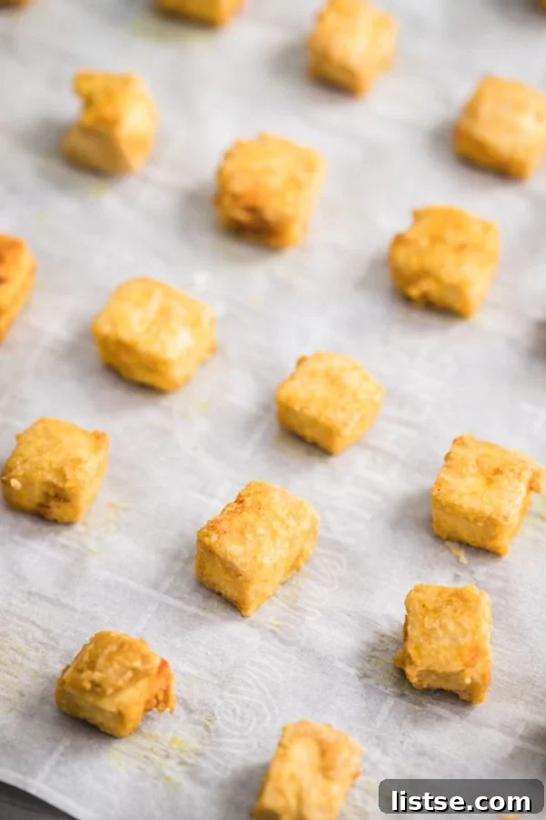 Crispy Golden Tofu Perfection 3 crispy cubes of tofu lined up on a baking sheet that's lined with parchment paper