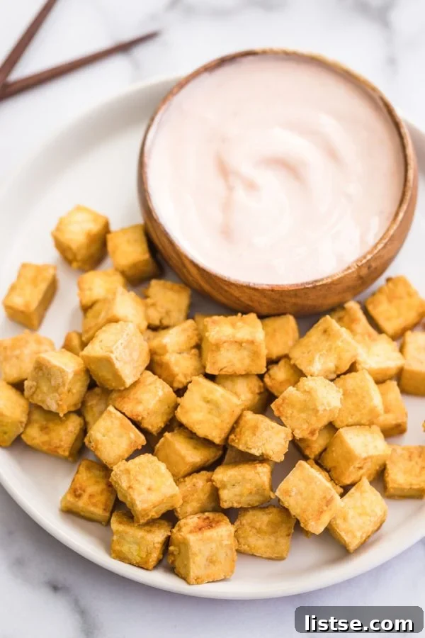 Crispy Golden Tofu Perfection 4 large plate filled with crispy breaded tofu cubes and with a wooden bowl of sauce on the side