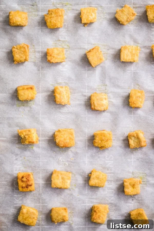 Crispy Golden Tofu Perfection 5 top down shot of crispy cubes of tofu lined up on a baking sheet that's lined with parchment paper