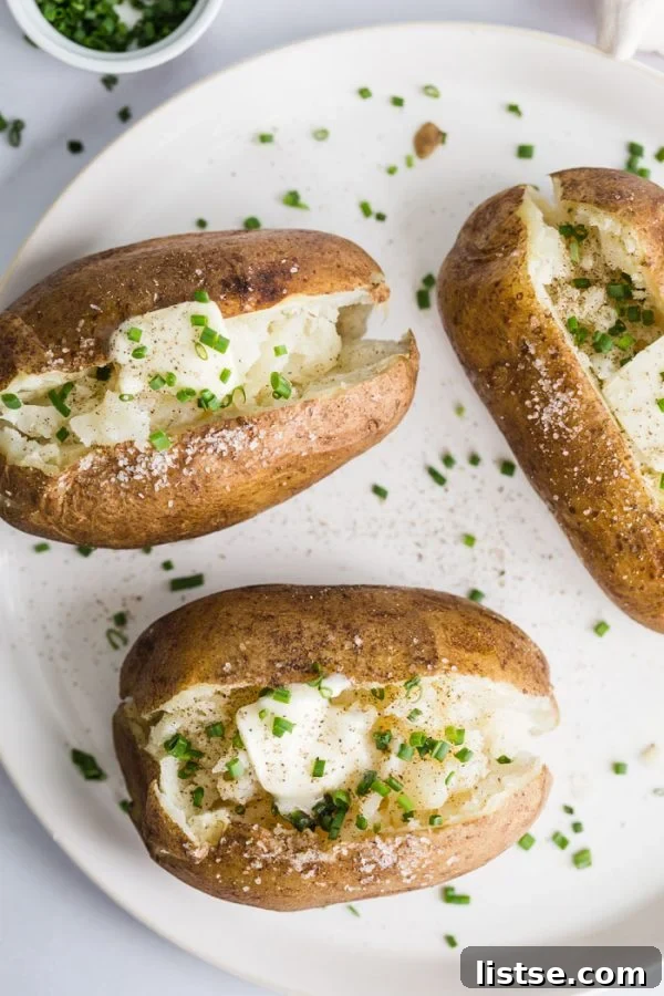 Fluffy Instant Pot Baked Potatoes 5 A beautifully plated serving of Instant Pot baked potatoes, each split open and generously topped with butter and fresh chives, highlighting their fluffy texture.