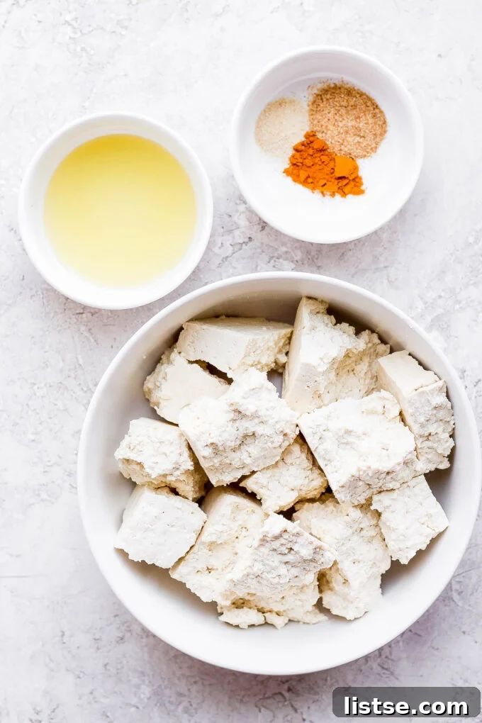 Effortless Vegan Scramble 4 A bowl of firm tofu chunks next to a separate bowl of seasoning blend, prepared for making a flavorful tofu scramble.