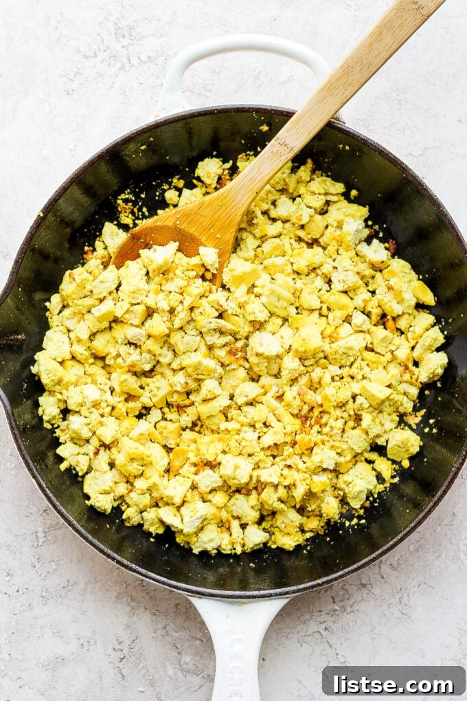 Effortless Vegan Scramble 6 Tofu being actively scrambled in a skillet with seasonings, developing a vibrant yellow color and an appetizing texture.