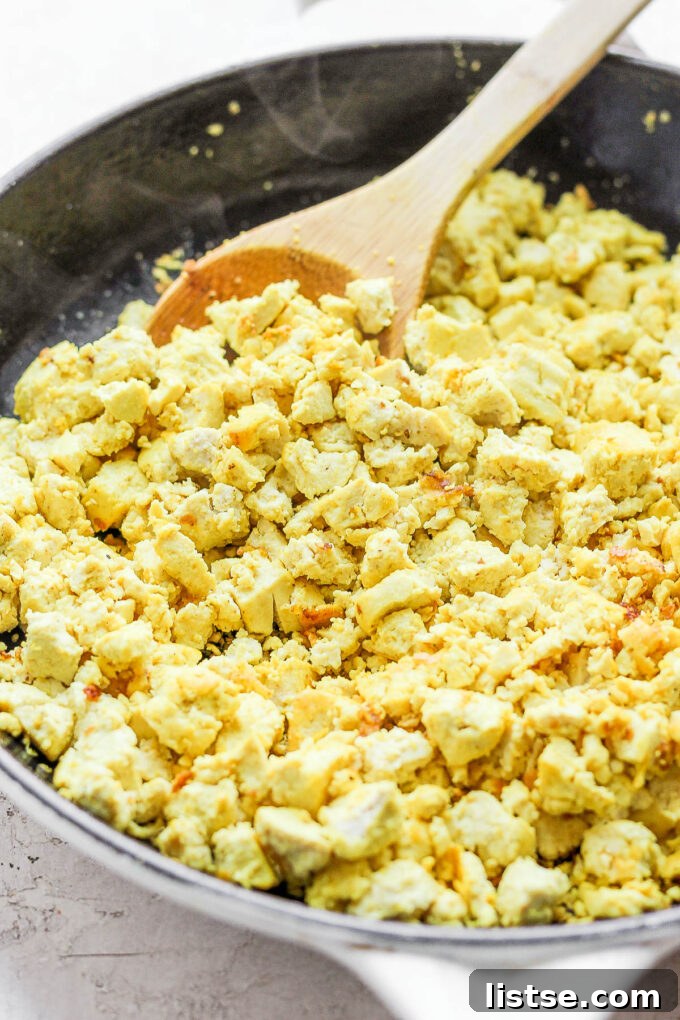 Effortless Vegan Scramble 7 Close-up view of tofu scramble being stirred in a skillet with a wooden spoon, showcasing its fluffy, egg-like consistency.