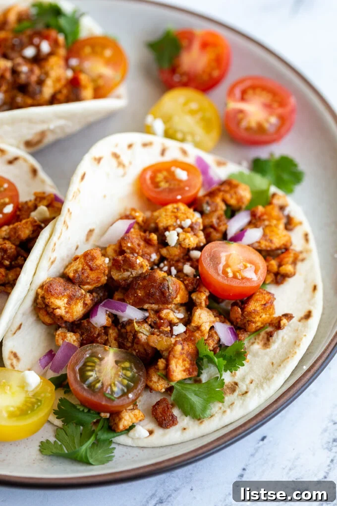 Effortless Tofu Taco Bliss 2 Fluffy flour tortilla filled with savory tofu taco meat, garnished with fresh cherry tomatoes, vibrant cilantro, finely diced red onion, and crumbled vegan feta.