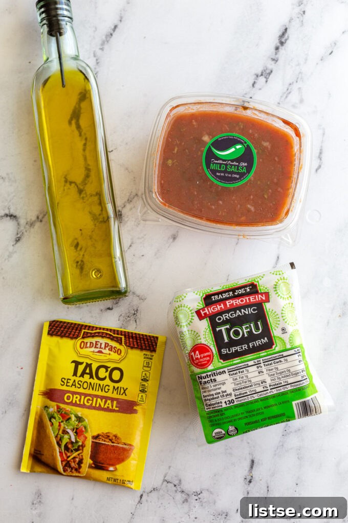 Effortless Tofu Taco Bliss 4 Simple ingredients laid out to make tofu tacos: a block of firm tofu, a bottle of olive oil, a jar of vibrant salsa, and a packet of taco seasoning, ready for preparation.