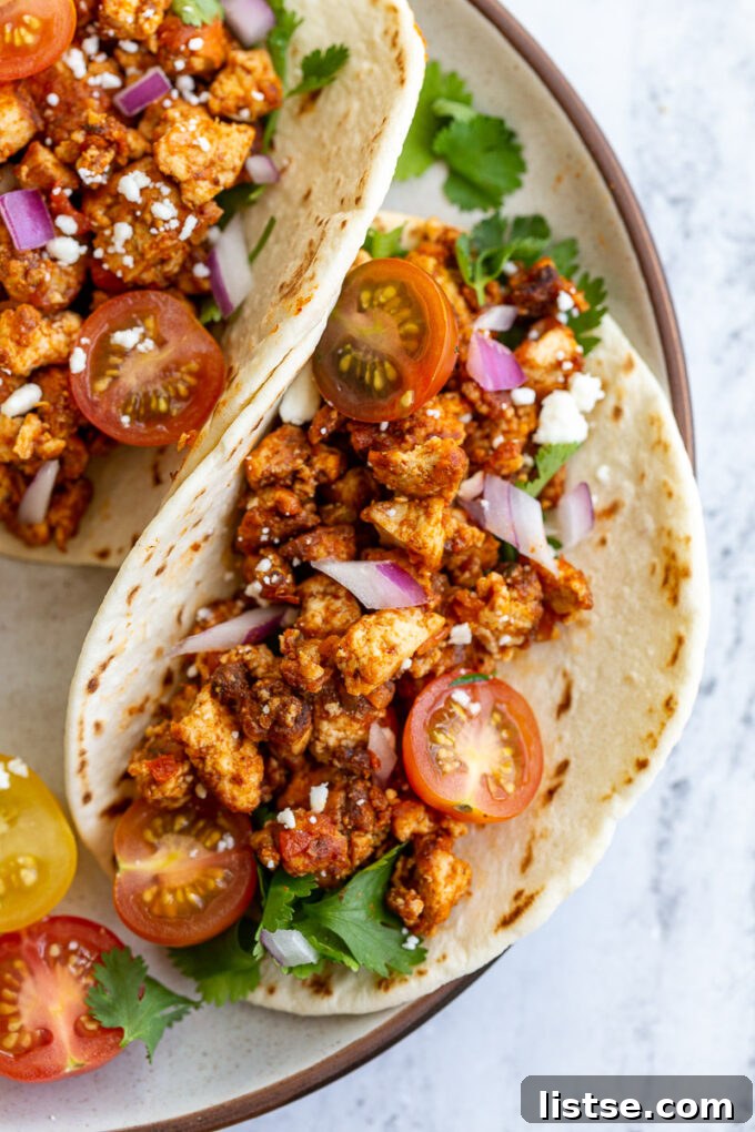 Effortless Tofu Taco Bliss 8 A vibrant and fully assembled flour tortilla taco, brimming with seasoned tofu taco meat and a colorful assortment of fresh toppings including cherry tomatoes, cilantro, and red onion, ready to be enjoyed.