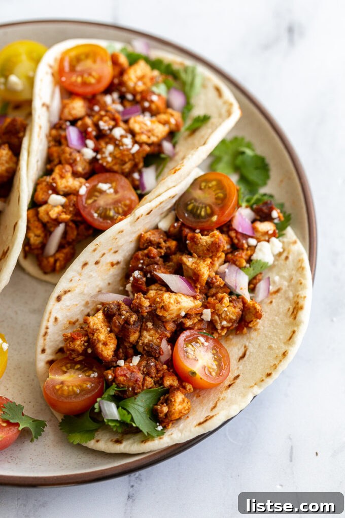 Effortless Tofu Taco Bliss 9 A trio of beautifully presented flour tortillas filled with savory tofu taco meat, garnished with fresh cherry tomatoes, vibrant cilantro, crisp red onion, and crumbled vegan feta cheese, arranged on a rustic wooden board.