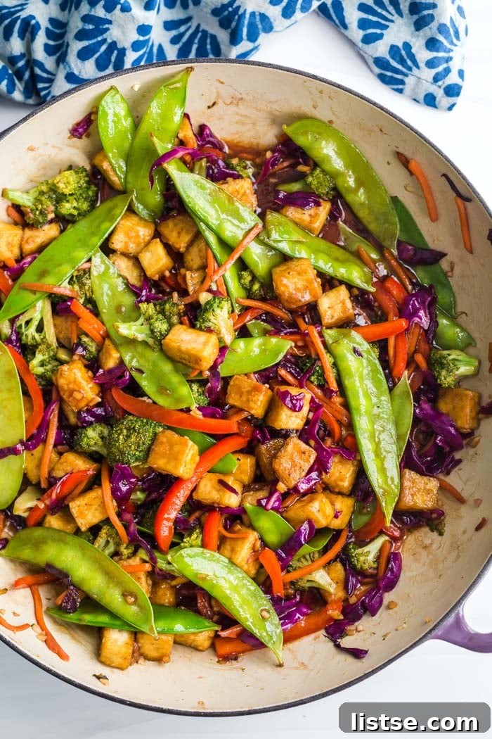 Tofu and vegetable stir fry sizzling in a large non-stick skillet on the stovetop.