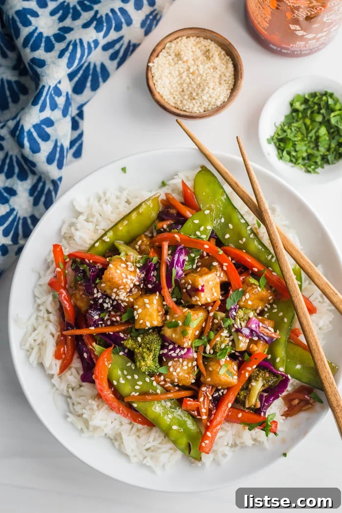 A generous serving of tofu stir fry over fluffy white rice, presented on a minimalist white plate.