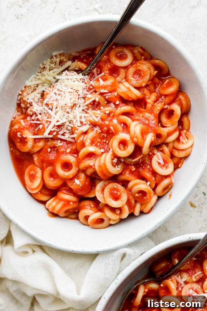 DIY Pasta Hoops 3 A serving of homemade spaghettios in a white bowl, generously topped with grated Parmesan cheese.