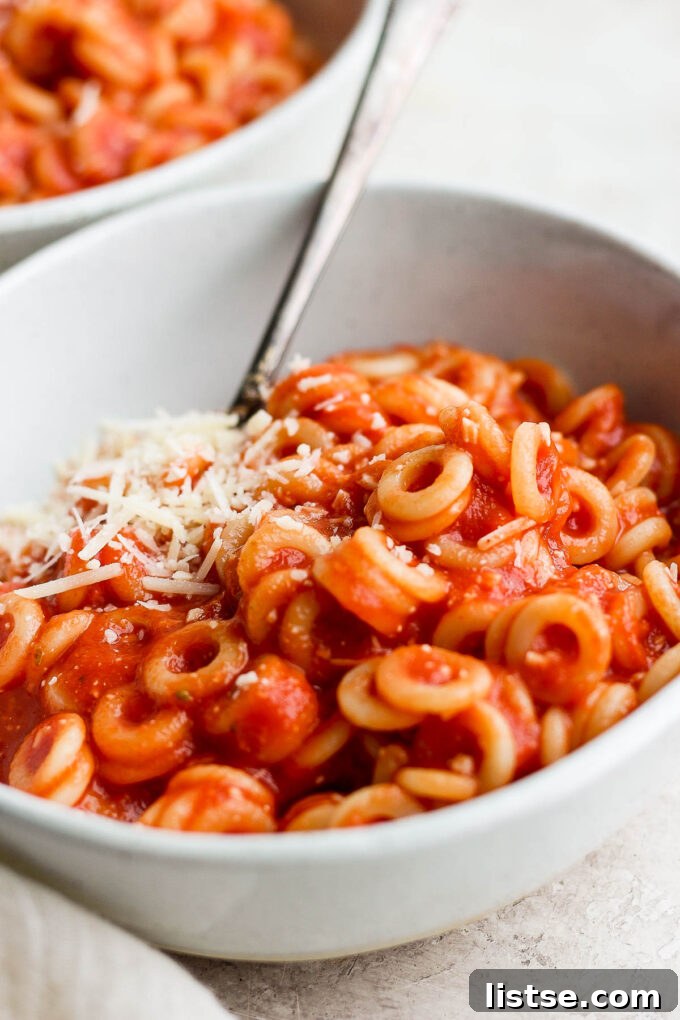 DIY Pasta Hoops 8 A white bowl filled with homemade spaghettios, accompanied by a spoon, highlighting its creamy texture.