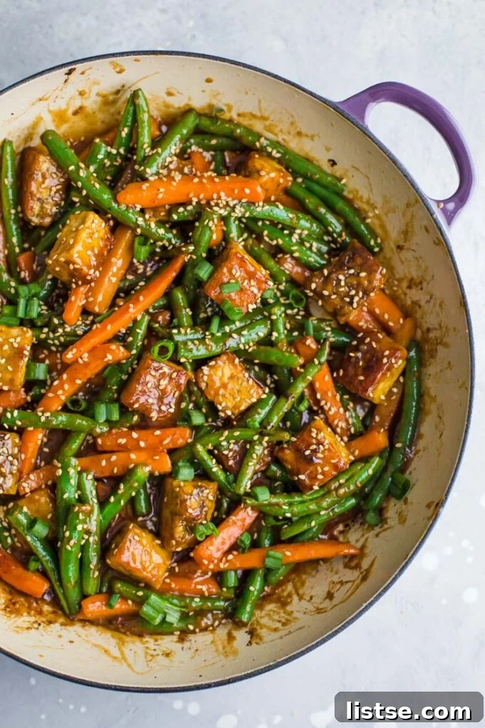 Tempeh stir fry with green beans and carrots in a large skillet, topped with sesame seeds, a fresh and healthy dinner.