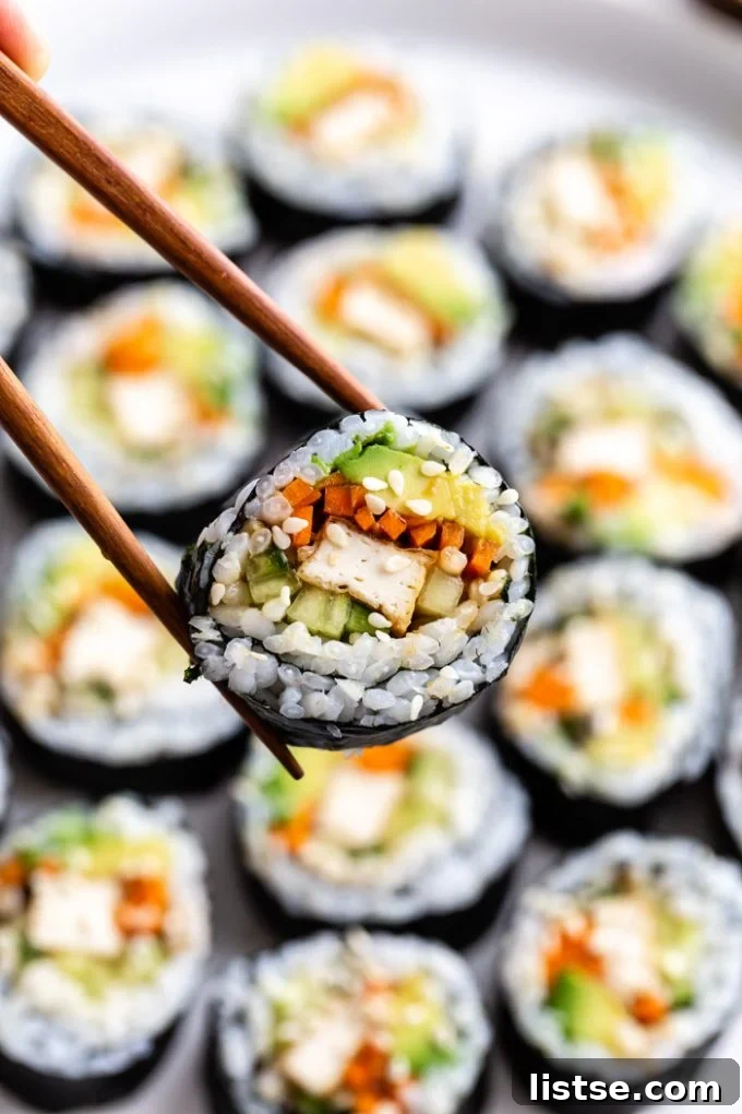 Sushi slice being held up to the camera with more in the background, showing homemade vegan sushi.