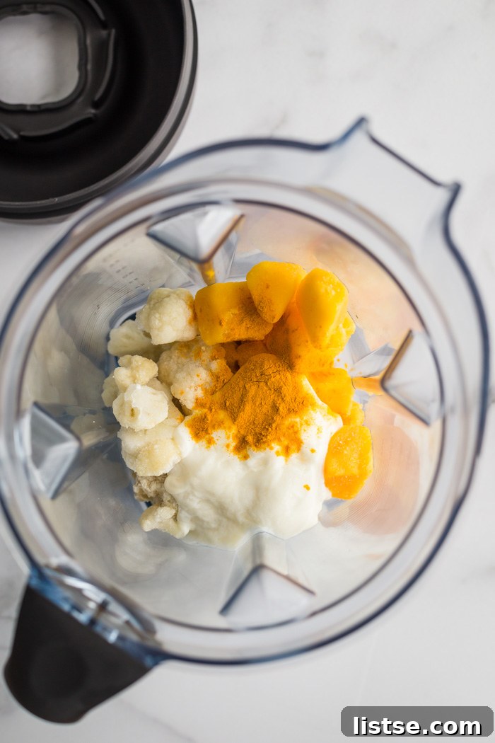 Overhead shot of mango smoothie ingredients including frozen mango, frozen cauliflower, yogurt, and turmeric powder, ready to be blended.