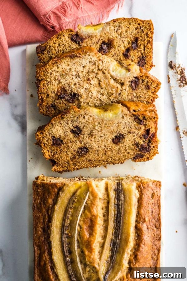Rich chocolate chip vegan banana bread slices on a marble board, garnished with a ripe banana and chocolate chips, ready to be enjoyed.