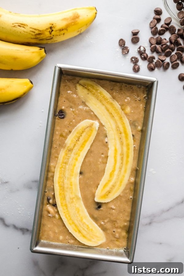 A close-up shot of the top of a vegan chocolate chip banana bread loaf, adorned with beautiful sliced banana halves, showcasing its moist texture.