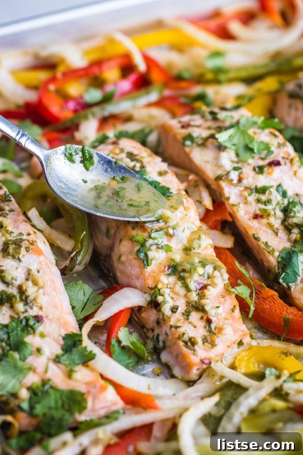 Sheet Pan Garlic Lime Salmon with colorful bell peppers and red onion, garnished with fresh cilantro and lime wedges.