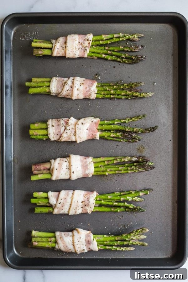 A close-up of bacon wrapped asparagus, seasoned and ready for cooking
