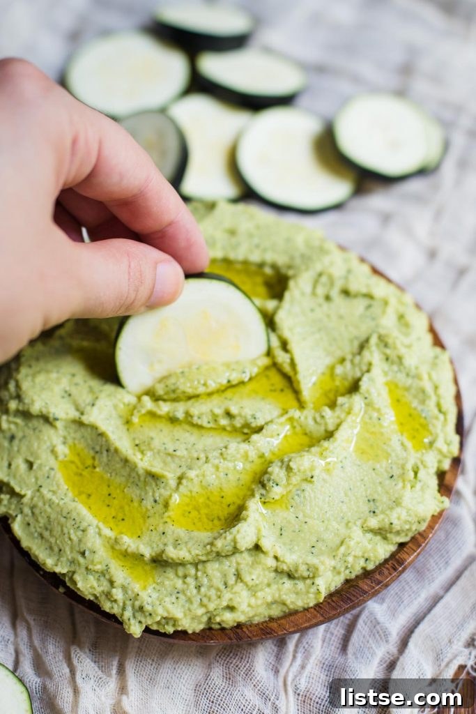 Bowl of light green zucchini hummus with fresh herbs and pita