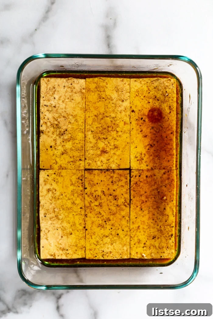 Flavorful Grilled Tofu 4 Close-up shot of raw tofu slices soaking in a rich, amber-colored marinade, absorbing all the aromatic spices and savory liquids before being grilled.