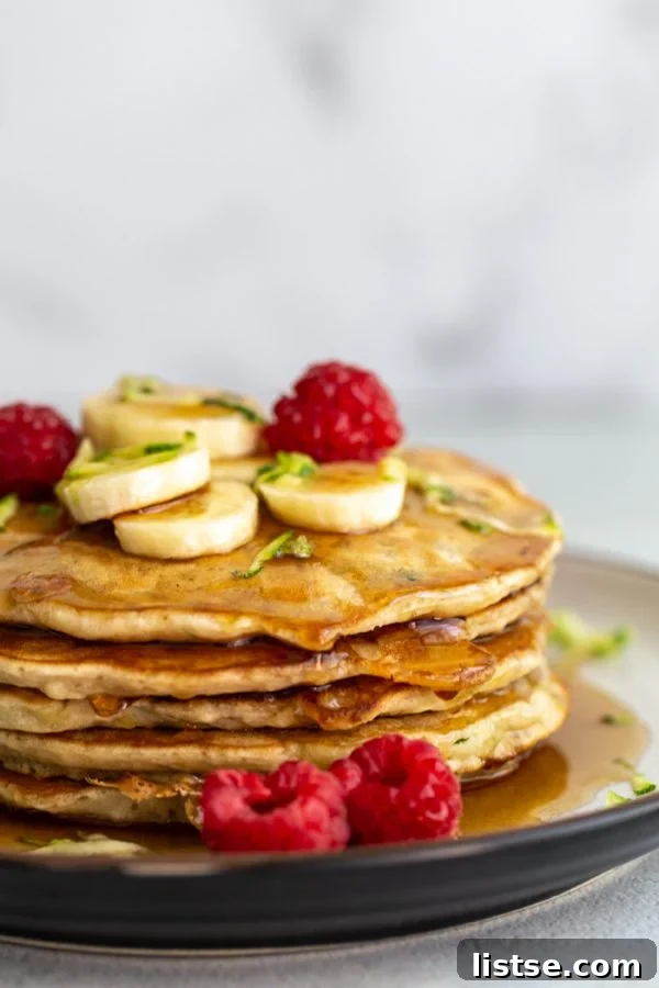 Savory Zucchini Fritters 5 A stack of golden-brown vegan zucchini pancakes, drizzled with maple syrup and garnished with fresh blueberries.