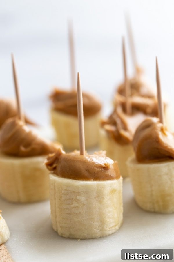Chocolate covered banana bites with peanut butter, topped with crushed peanuts, on parchment paper.