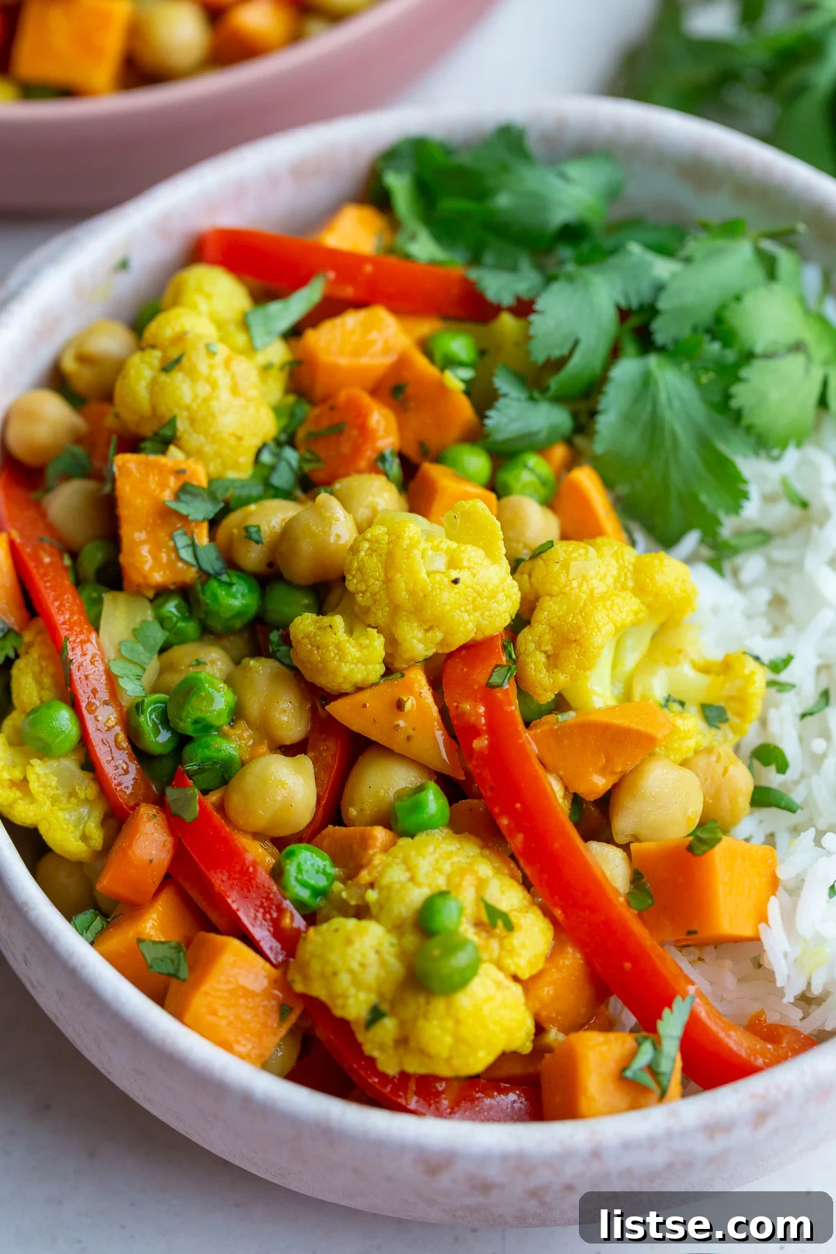 Golden Vegan Chickpea and Sweet Potato Coconut Curry 4 A bowl of sweet potato chickpea curry served over white rice, garnished with fresh cilantro and a lime wedge.