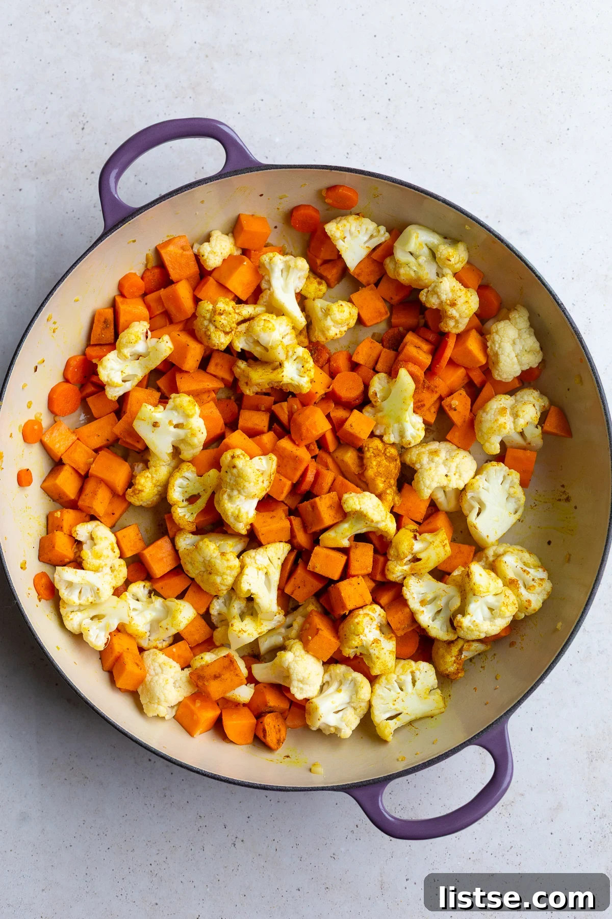 Golden Vegan Chickpea and Sweet Potato Coconut Curry 5 Diced sweet potato, cauliflower florets, and sliced carrots cooking in a skillet with fragrant curry powder.
