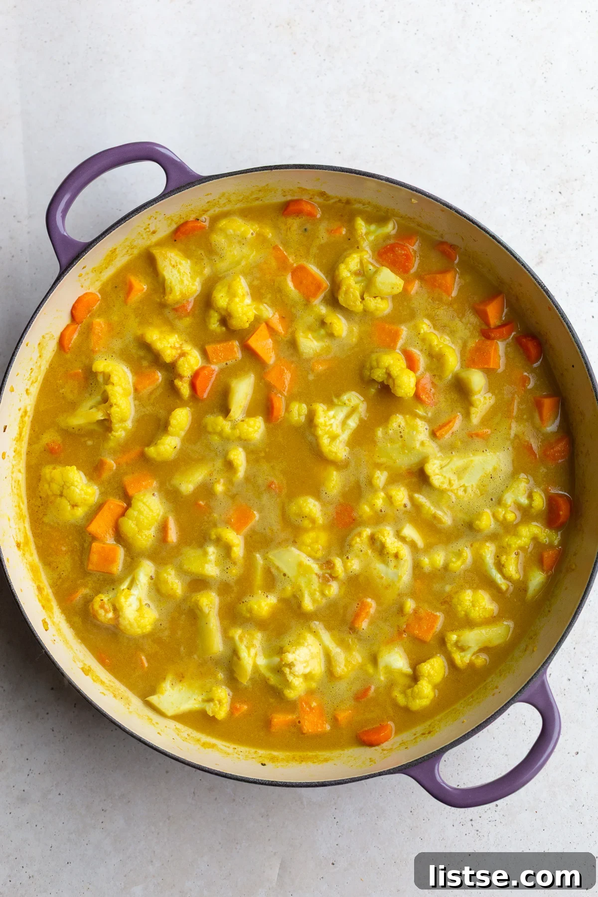 Golden Vegan Chickpea and Sweet Potato Coconut Curry 6 The cooking cauliflower and carrot curry in a skillet, with liquids and spices already added, creating a rich sauce base.