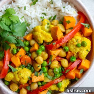 Golden Vegan Chickpea and Sweet Potato Coconut Curry 10 chickpea and sweet potato curry in a bowl that also has red pepper and peas in in served on white rice with cilantro on the side