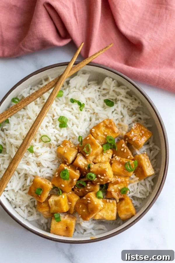sauteed tofu on a bed of rice and topped with green onion and sesame seeds. on a marble board with a pink towel in the corner