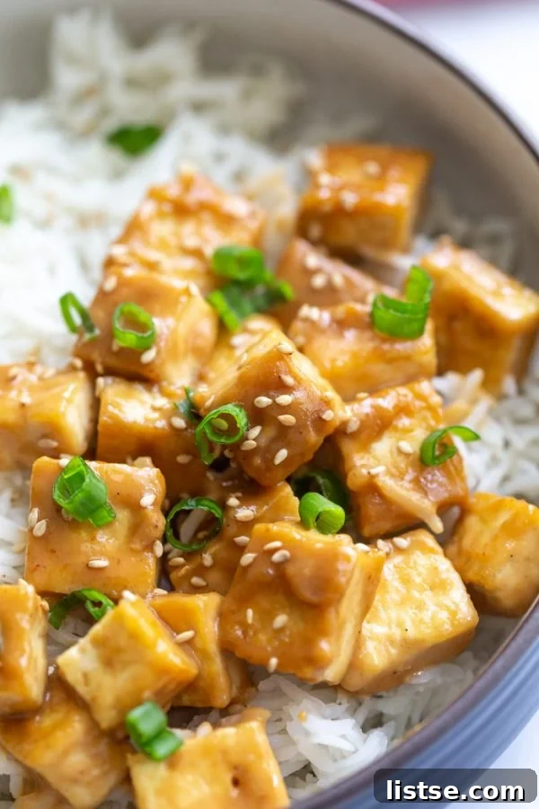 up close shot of perfect sauteed tofu on a bed of rice and topped with green onion and sesame seeds. on a marble board with a pink towel in the corner