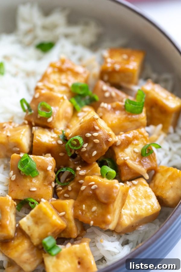 Tofu cubes on a bed of white rice, generously covered in a rich brown tahini sauce and garnished with sliced green onions and sesame seeds.