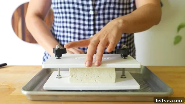 Someone placing a block of tofu into a white tofu press, which is sitting on a baking sheet to catch excess liquid.
