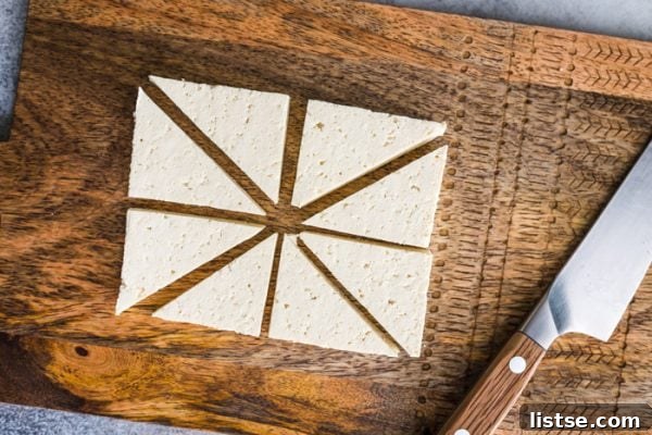 Overhead shot of firm tofu cut into uniform triangles, resting on a wood cutting board with a knife nearby.