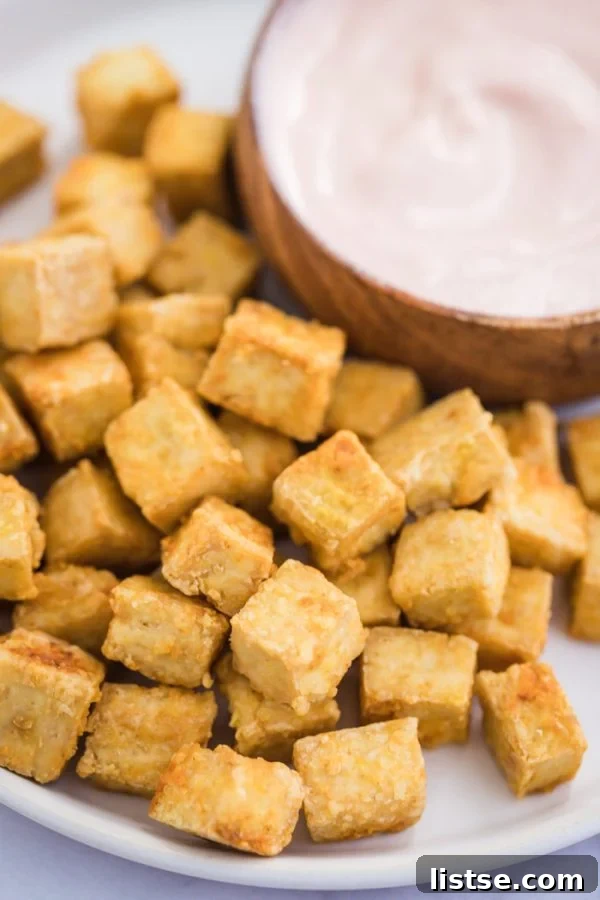 Side shot of perfectly crispy baked tofu cubes piled on a white plate, ready to be served.