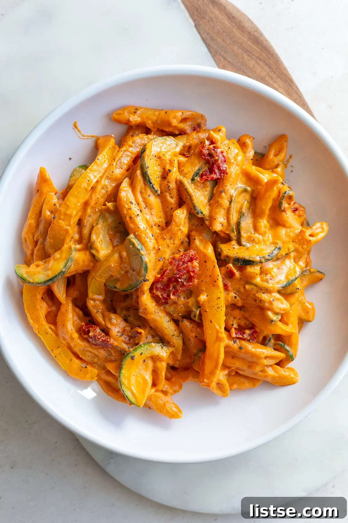Creamy tomato pasta served in a white bowl, garnished with fresh herbs.