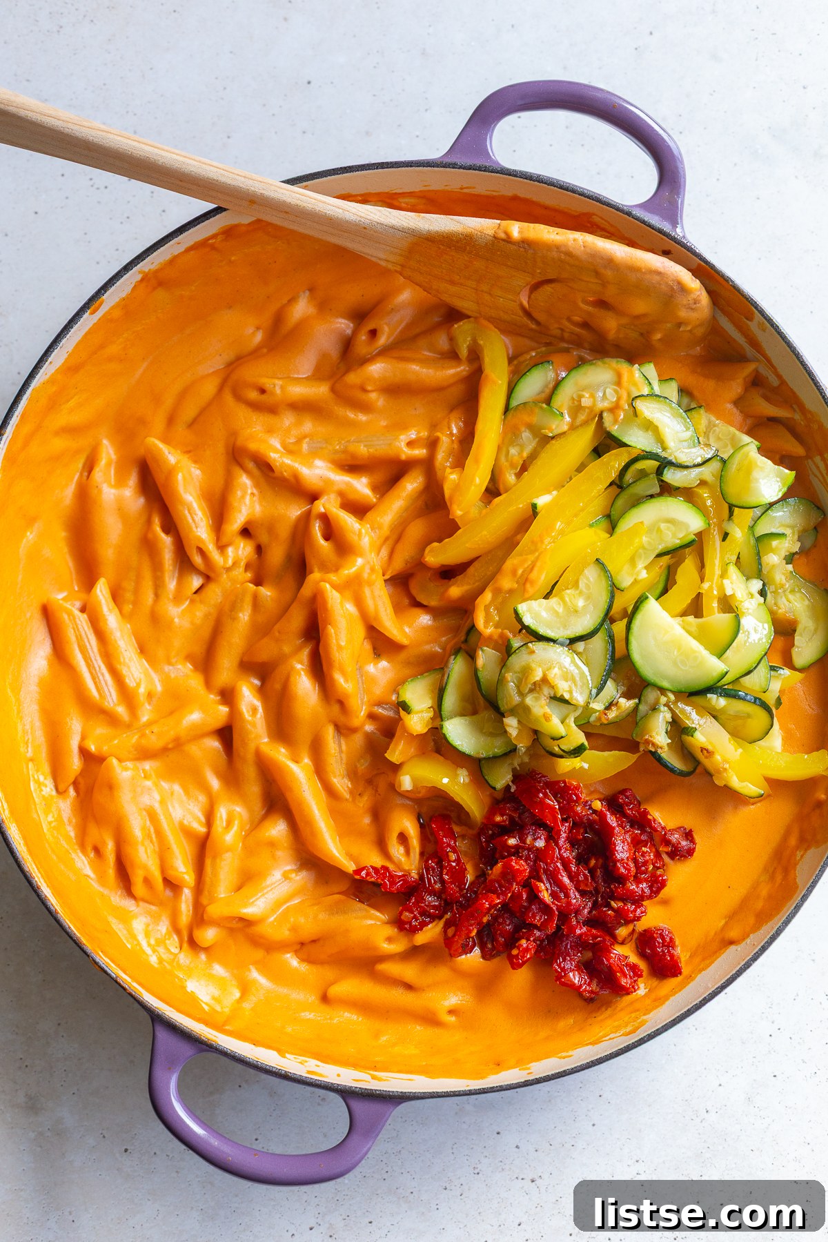 Stirring together creamy tomato sauce, water, and penne pasta in a skillet.