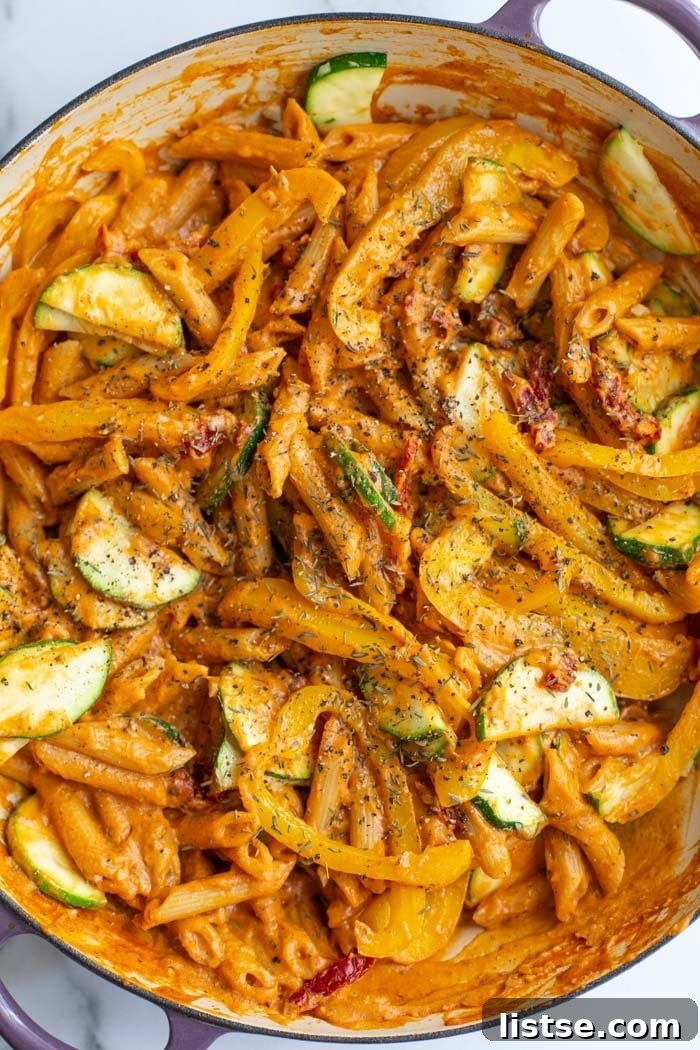 Creamy tomato pasta with zucchini and bell peppers topped with fresh basil in a white bowl.
